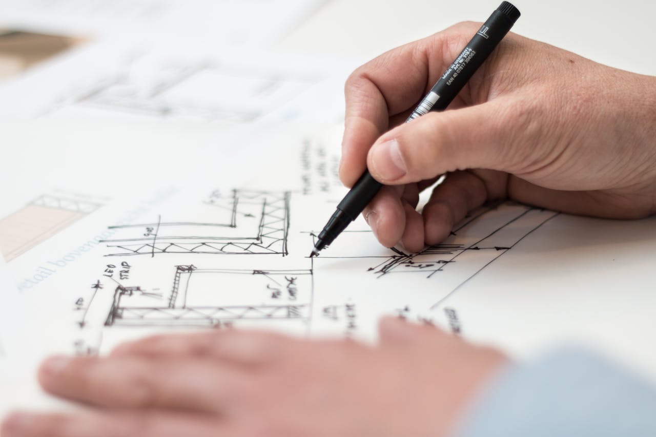 heros-img Close-up of hand drawing intricate technical designs on blueprint with pen, ideal for engineering or architecture themes.
